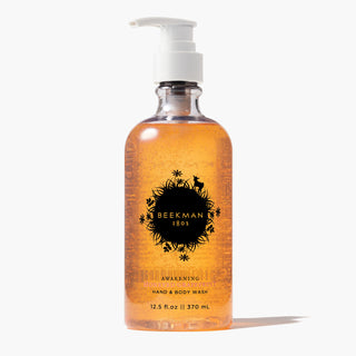 Clear bottle of Beekman 1802's Honeyed Grapefruit Hand & Body Wash with a white nozzle standing on a white background. 