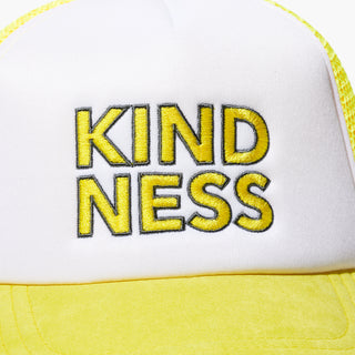 Up close shot of the front of the Beekman 1802's Kindness Trucker Hat, showing the word "Kindness" in yellow block letters on the white part of the hat.