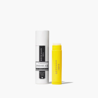 Yellow uncapped tube of Beekman 1802's Fresh Air Lip Balm standing next to the white packaging tube that says Fresh Air on the front, on a white background. 