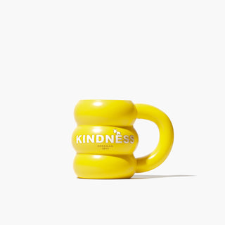 Beekman 1802's Yellow Sunshine Ceramic Doughnut Mug which has the word "Kindness" in white block letters and a goatie on the front of the mug, on a white background.