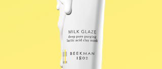 Up close image of Beekman 1802's Milk Glaze Deep Pore Purging Lactic Acid Clay Mask with product dripping down tube and on a yellow background.