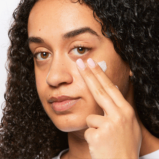 GIF of model applying Beekman 1802's Bloom Cream daily moisturizer onto her face with her fingers and looking at the camera. 