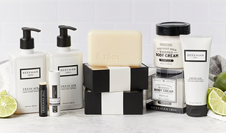 Products from Beekman 1802's Fresh Air collection all displayed together showing the bar soaps, body cream, hand & Body wash, hand cream, lotion and lip balm, surrounded by limes on a light gray tile background.  