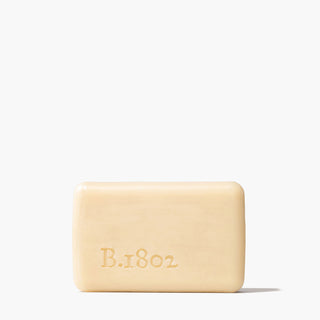 Unwrapped nude bar of Beekman 1802's goat milk 9 ounce bar soap standing on a white background, next to shadow.