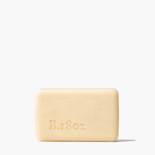 Unwrapped bar of Nectarine Hibiscus Goat Milk Soap which has the word "B.1802" stamped on the bottom left of the soap, standing on a white background.