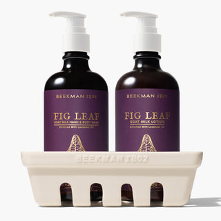 Beekman 1802's fig leaf caddy set which shows bottles of hand and body wash on the left and lotion on the right, both with white nozzles and standing inside a ceramic caddy that says "beekman 1802" on the front, all on a white background.