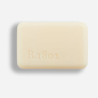 Unwrapped bar of Beekman 1802's Jasmine Bloom Goat Milk Soap on a grey background.