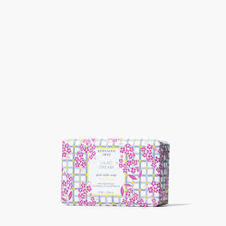 Paper-wrapped bar of Beekman 1802's Lilac Dream Goat Milk Soap, which has gingham and lilac flowers on the packaging, standing on a white background.