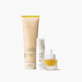 Beekman 1802's Brighter Days Skincare Set which includes milk scrub, mini bloom cream, and golden booster all lined up next to each other on a light gray background.