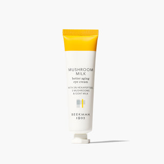 White tube of Beekman 1802's Mushroom Milk Better Aging Eye Cream that is yellow on the sealed end of the tube, standing on a white background.