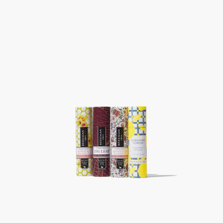 4 lip balms from Beekman 1802's Blowing Kisses 4-Piece Lip Balm Set, all lined up next to each other on a grey background.