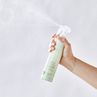 Close up shot of hand holding the Beekman 1802 Goat Milk Hair Mist and spraying it directly into the air. 