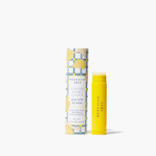 Tube of Beekman 1802's yellow goat milk lip balm standing next to lip balm packaging, on a white background.