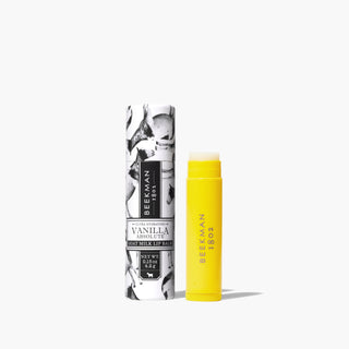 Yellow tube of Beekman 1802's Vanilla Absolute Lip Balm, standing next to black and white packaing tube for lip balm thats covered in goats, on a white background.