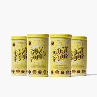 Four Yellow tin of Beekman 1802's 2023 Goat Poop Ultra Premium Chocolates which says "goat poop" on the front and images of chocolate pieces, all lined up next to each other on a white background.
