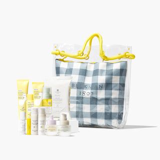 Beekman 1802's Mini Miracle Set which features 10 mini, travel-sized skincare products all grouped together in front of a gingham tote bag with yellow hands, on a gray background.
