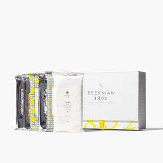 Shot of all 6 face wipes that are a part of Beekman 1802's Sweet to be kind 6-piece face wipes set which are all lined up next to each other, in front of a white gift box that has an image of a cartoon goatie in the front with the words "Beekman 1802" under it, on a white background.