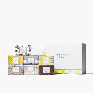 Set of eight Beekman 1802 goat milk bar soaps all stacked on top of each other next to a white gift box that says "beekman 1802" on the front, on a white background.