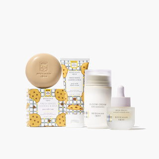 Products from Beekman 1802's Milk & Cookies Beauty Gift Set, which includes the Nestle Toll House fresh baked cookies and milk round bar soap and hand cream, and the regular size bloom cream daily moisturizer and bottle of milk drops serum, on a white background. 