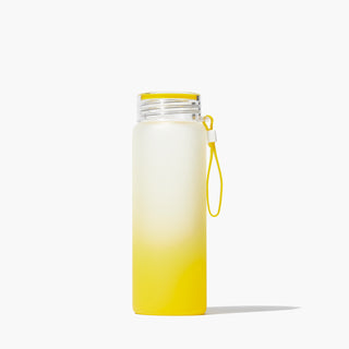 Beekman 1802's Glass Water Bottle which has a frosted yellow color gradient from the bottom to top of the bottle, and a rubber wrist carrier attached to the side on a white background.