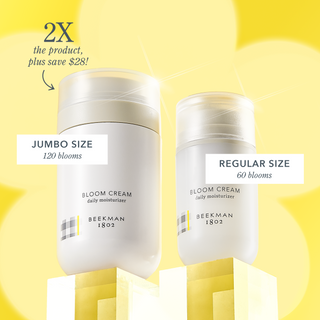 Size comparison image of bottles of the jumbo size bloom cream and the regualar size bloom cream, with the jumbo size on the left with the label "jumbo size: 120 blooms" and an arrow pointing to it saying "2x the product, plus save $29!" and the regular size on the right with a label that says "regular size: 60 blooms" all on a yellow background.