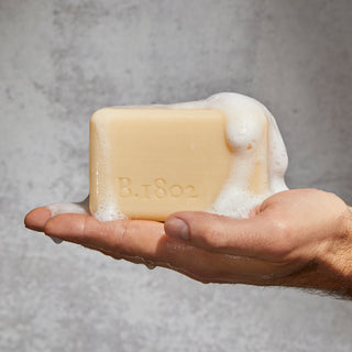 Hand holding a bar of soap with soap suds falling off the soap. 