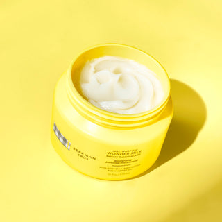 An image of the beekman 1802 Multipurpose wonder milk butter botanical jelly with the lip off and showing the product inside on a yellow background.