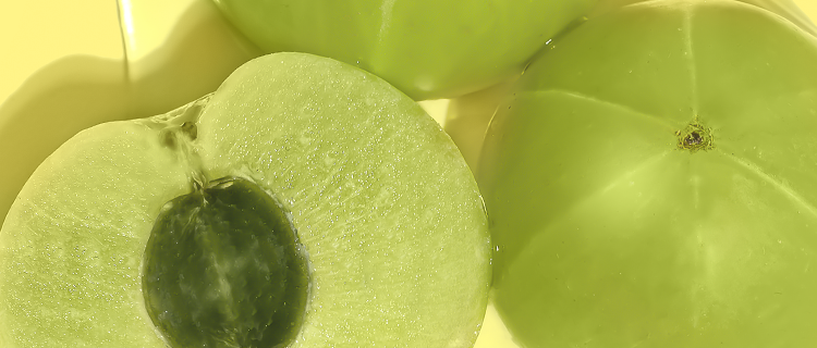 Close up shot of 2 full green amla berries and one split in half showing the cross section, on a yellow background. 