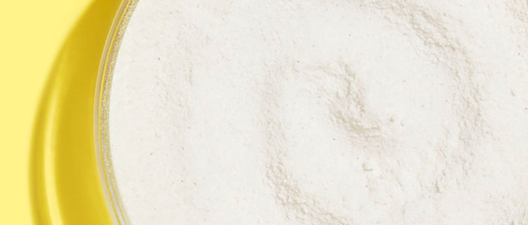 Up close shot of white mineral zinc oxide ingredient powder in a clear petri dish on a yellow background.