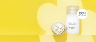 One pack of Bloom Cream standing and one laying down showing bloom cream goop on yellow background as a flower