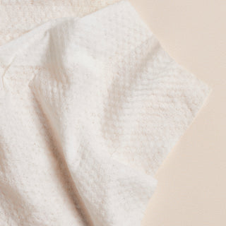 Up close shot of Beekman 1802's Supersized Pure goat milk Face Wipes towelette, on an eggshell colored background.