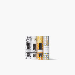 4 lip balms all lined up next to each other that come in Beekman 1802's Under the Mistletoe 4-Piece Lip Balm Set, which shows Vanilla Absolute, Pure, Honey & Orange Blossom, and lavender lip balms from left to right, on a white background.
