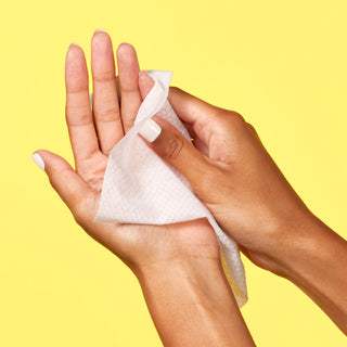 Up close shot of hand wiping the other hand with Beekman 1802's Lilac Dream Face Wipes, on a yellow background.