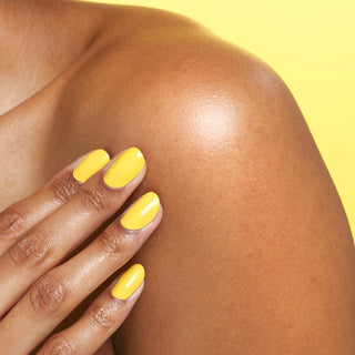 Up close shot of moisturized, hydrated shoulder after using Beekman 1802's Lilac Dream Whipped Body Cream, with model's hand that's wearing yellow nail polish touching their shoulder on a yellow background.