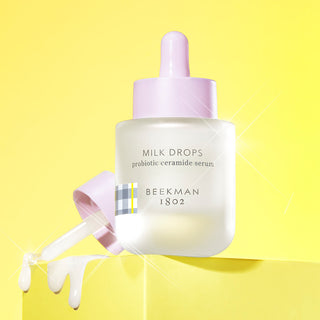 Milk Drops serum on a stand with dropper leaking white serum drops 