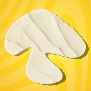 Texture swatch of Beekman 1802's Mushroom Milk Better Aging Eye Cream in the shape of a mushroom on a yellow background.