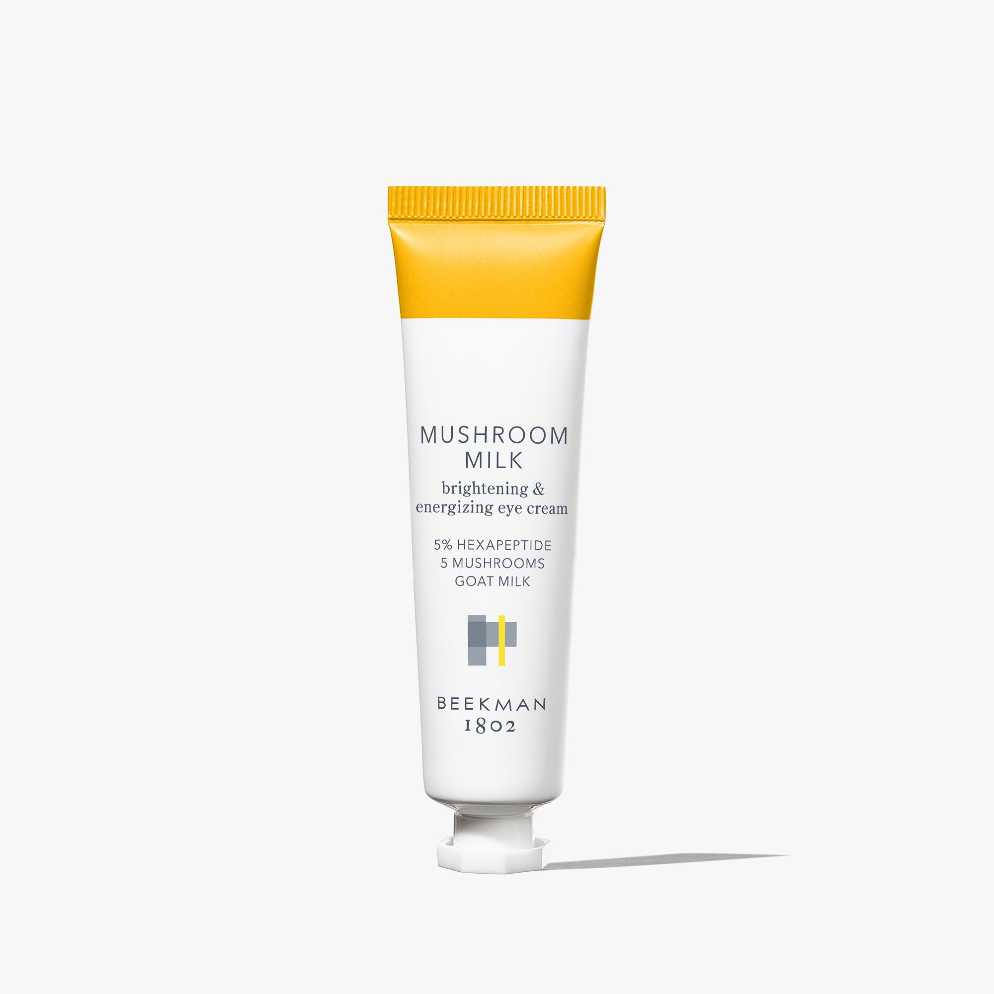 White tube of Beekman 1802's Mushroom Milk Better Aging Eye Cream that is yellow on the sealed end of the tube, standing on a white background.