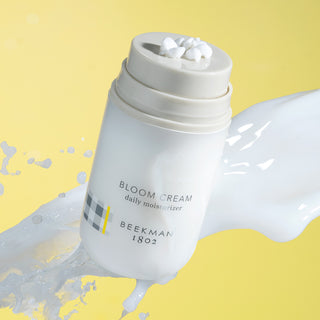 Pack of Bloom Cream Daily Moisturizer shown in front of yellow background with splash of goat milk 