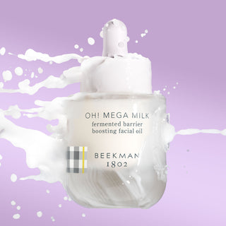Bottle of Beekman 1802's Oh! Mega Milk Fermented Barrier Boosting Facial oil in the air with milk splashing onto it on a purple background.