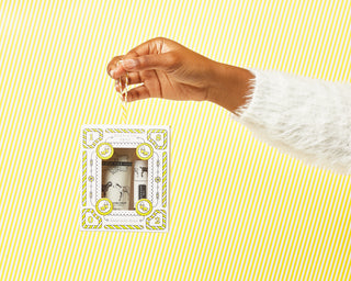 Hand holding the box of Beekman 1802's Pure Hand & Lip Hydration Kit, on a white and yellow striped background.