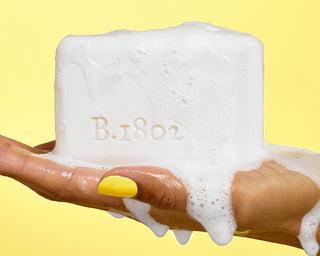 Hand model holding a 9oz goat milk bar soap on yellow background