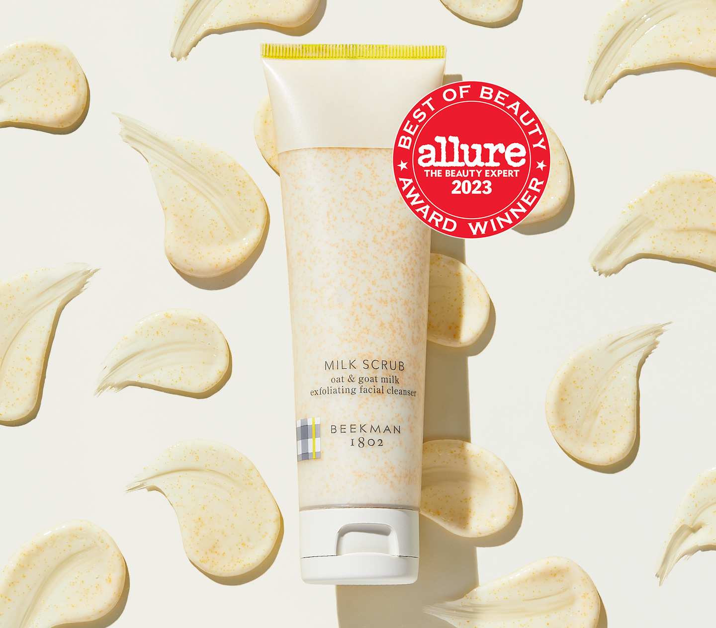 Tube of Beekman 1802's Milk Scrub Oat + Goat Milk Exfoliating Cleanser on a eggshell background surrounded by product texture swatches, next to a red seal that says "Allure 2023 Best of Beauty Award Winner."