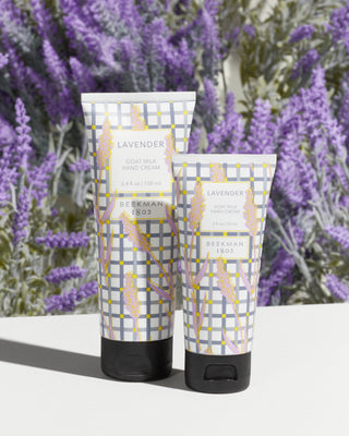2 Lavender Goat Milk Hand creams standing next to each other in sizes 3.4 ounce and 2 ounces with lavender flowers in the background. 