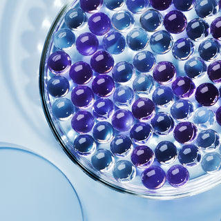 Close up shot of petri-dish filled with purple and blue ceramide gel orbs on a blue background. 