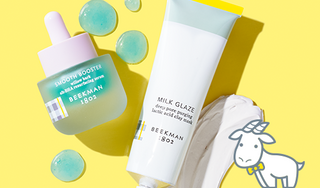 Bottle of Beekman 1802's Smoother Booster Willow Bark Resurfacing Serum and Tube of Beekman 1802's Milk Glaze Clay Mask surrounded by blue serum droplets and clay mask texture smear, on a yellow background next to white cartoon goatie to the right of the products.   