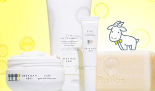 Products from Beekman 1802's Pure Fragrance-Free line which includes the whipped body cream, soap paste, cuticle serum, and goat milk soap all on a yellow background surrounded by bubbles, and an image of a white cartoon goatie standing on top the bar soap. 