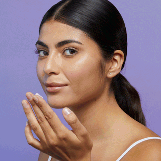 GIF of model applying Beekman 1802's Midnight Milk Better aging sleep mask, which is a light purple, onto her cheek and looking at the camera, on a purple background.