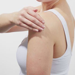 GIF of Models shoulder while wearing a white tank top and applying Beekman 1802's Nectarine HibiscusWhipped Body Cream to her arm and rubbing it down.