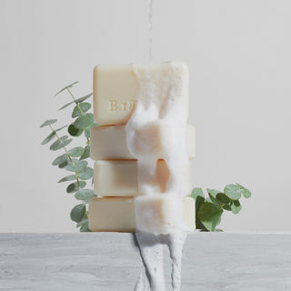Glacial Mint & Eucalyptus soap stacked with soap suds falling down them on a grey background with eucalyptus behind the stack. 