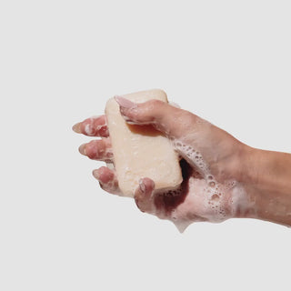 Video of hand holding and rubbing an unwrapped beekman 1802 Palm-Sized Goat Milk Soap which is wet and covered in suds.